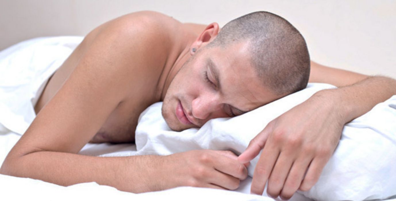 Mann mit rasiertem Kopf und nacktem Oberkörper schläft auf dem Bauch