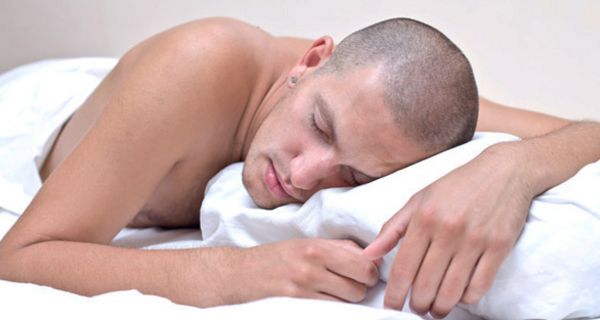Mann mit rasiertem Kopf und nacktem Oberkörper schläft auf dem Bauch