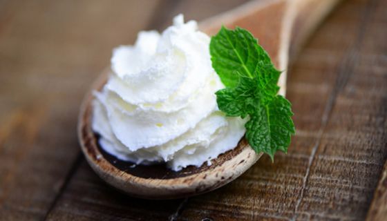 Foodpic: Nahaufnahme: Holzlöffel, darin Schlagsahne, als Deko Minzblatt, auf Holztisch