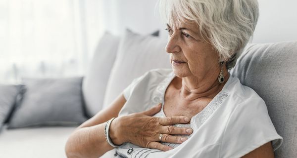 Ältere Frau, hält sich eine Hand an den Brustkorb.