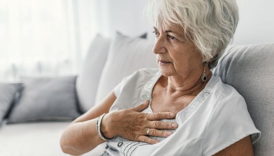 Ältere Frau, hält sich eine Hand an den Brustkorb.