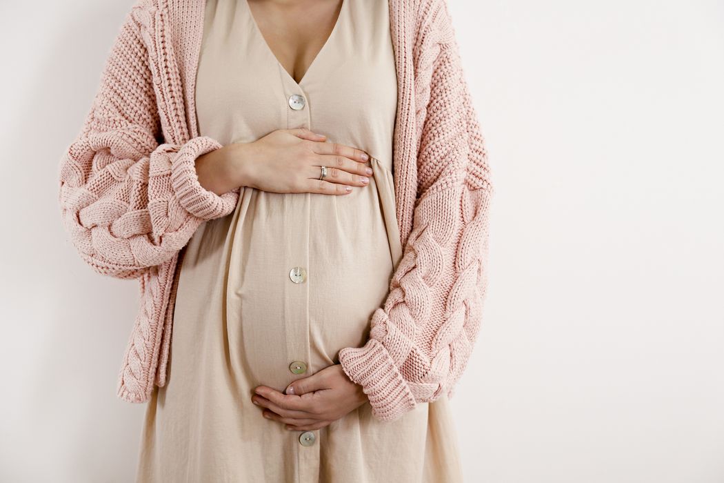 Schwangere Frau, hält eine Hand oben und eine unten an ihrem Bauch.