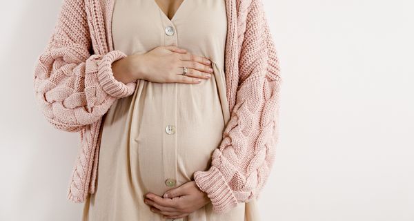 Schwangere Frau, hält eine Hand oben und eine unten an ihrem Bauch.