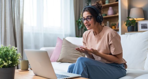 Junge Frau in weiten Kleidern mit Headset sitzt vor einem Laptop. Sie ist emotional aufgewühlt.