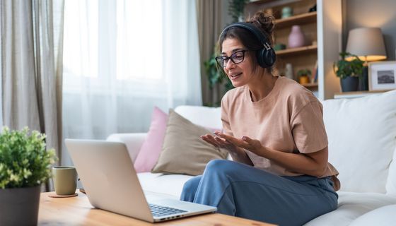 Junge Frau in weiten Kleidern mit Headset sitzt vor einem Laptop. Sie ist emotional aufgewühlt.