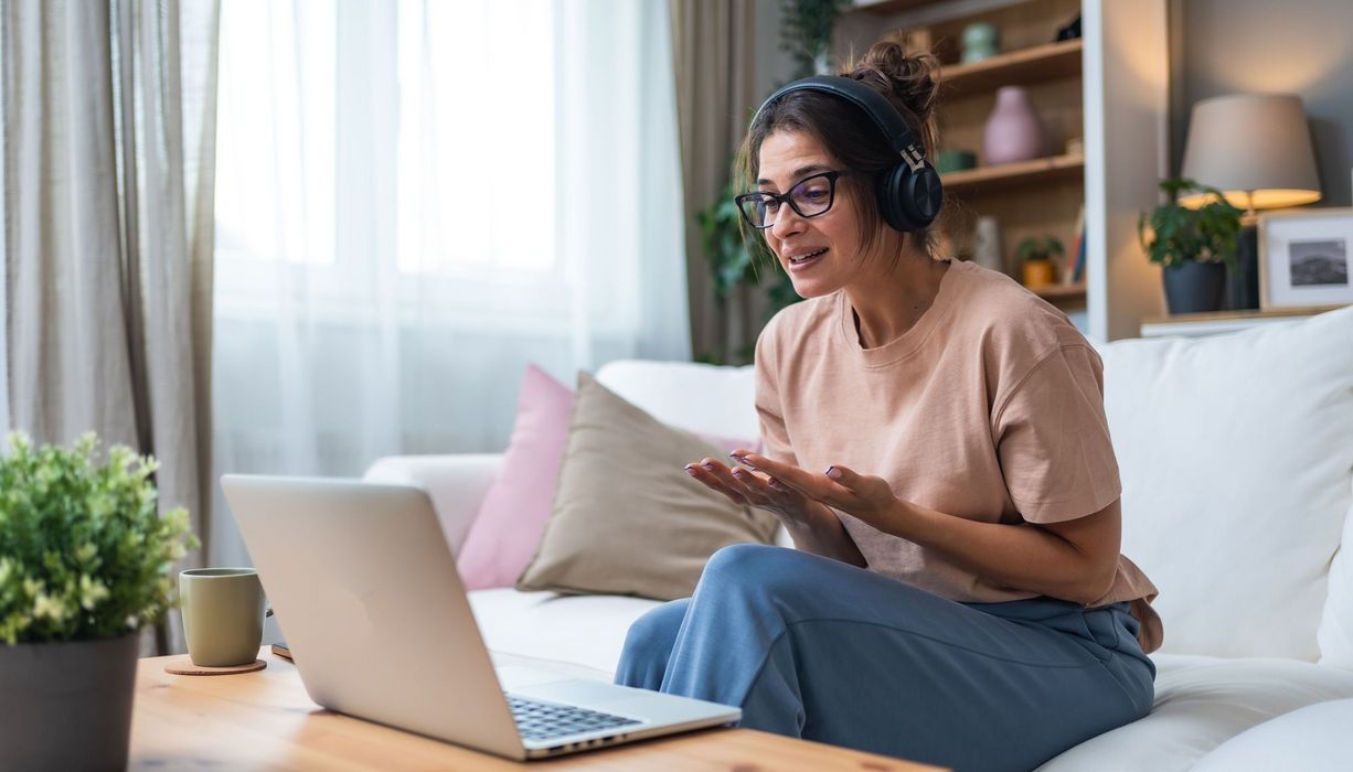 Junge Frau in weiten Kleidern mit Headset sitzt vor einem Laptop. Sie ist emotional aufgewühlt.