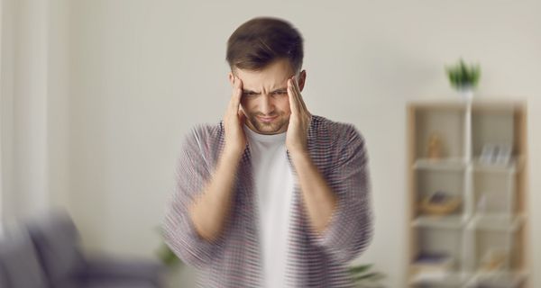 Mann fasst sich an die Schläfe und blickt nach unten. Im unteren Bereich ist das Bild verwischt, als hätte sich die Kamera schnell bewegt.