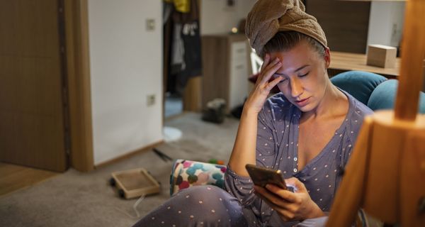 Junge Frau, zu Hause und krank, hält ihr Handy in der Hand.