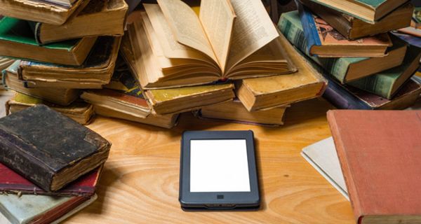 E-Book liegt auf einem Tisch inmitten von chaotischen Stapeln alter Bücher