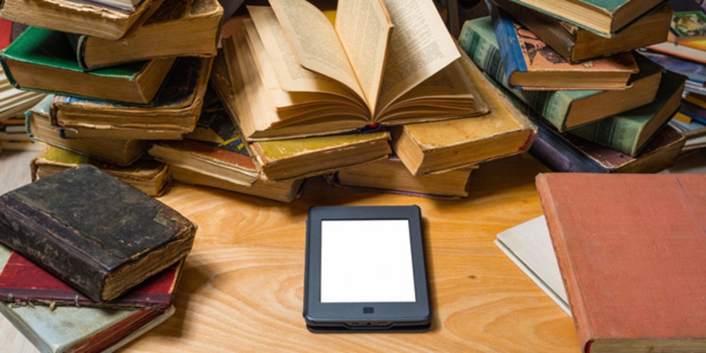 E-Book liegt auf einem Tisch inmitten von chaotischen Stapeln alter Bücher