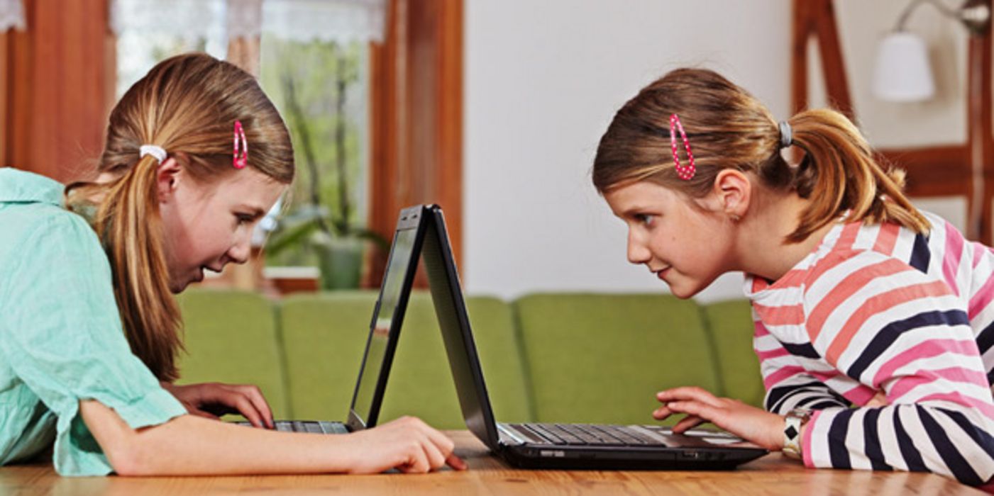 Zwei Mädchen sitzen sich mit Laptops gegenüber