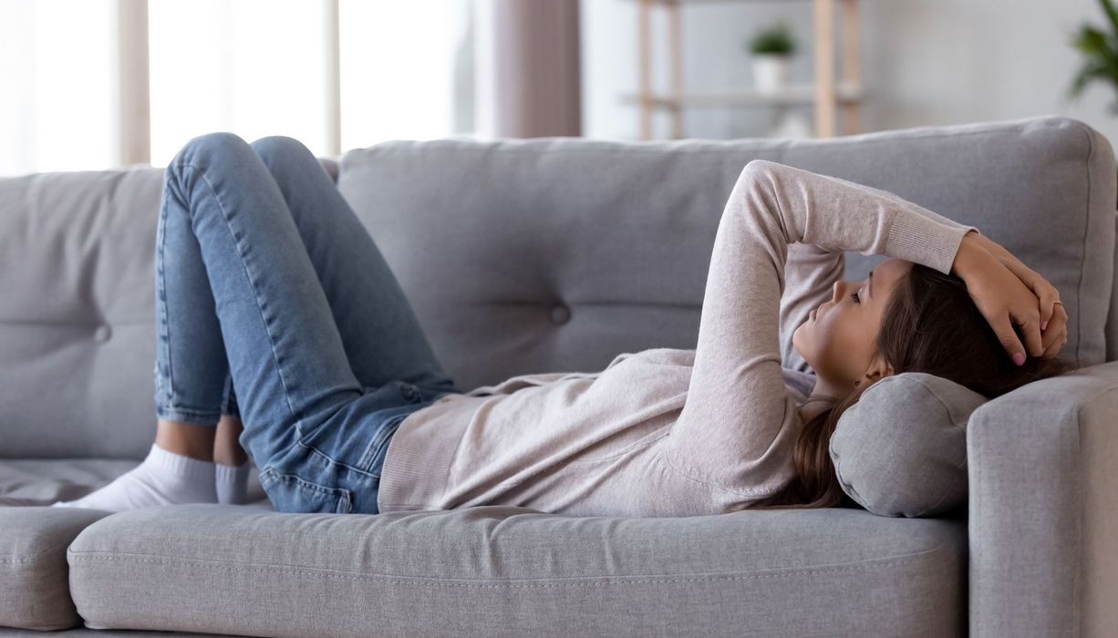 Junge Frau liegt erschöpft auf der Couch.