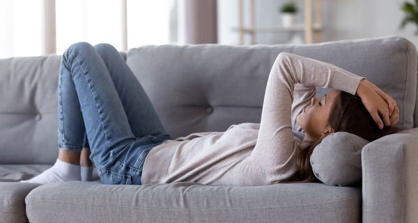 Junge Frau liegt erschöpft auf der Couch.