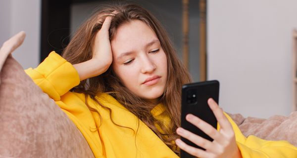 Jugendliche sitzt auf dem Sofa und ist am Smartphone. Sie blickt mäßig glücklich.