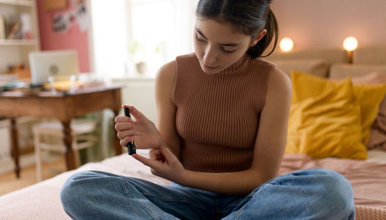 Jugendliche misst ihren Blutzuckerspiegel, während sie auf ihrem Bett sitzt.