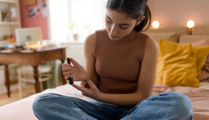 Jugendliche misst ihren Blutzuckerspiegel, während sie auf ihrem Bett sitzt.