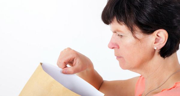 Ältere Frau zieht einen Brief aus einem Umschlag