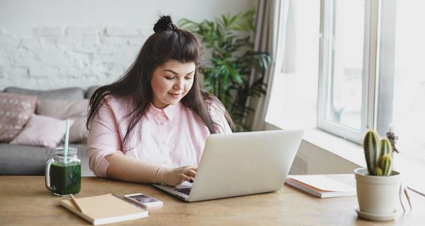 Eine übergewichteige junge Frau sitzt vor einem Laptop und tippt.