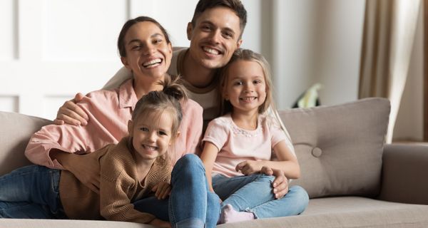 Junge Familie mit zwei Kleinkindern sitzt zusammen auf dem Sofa