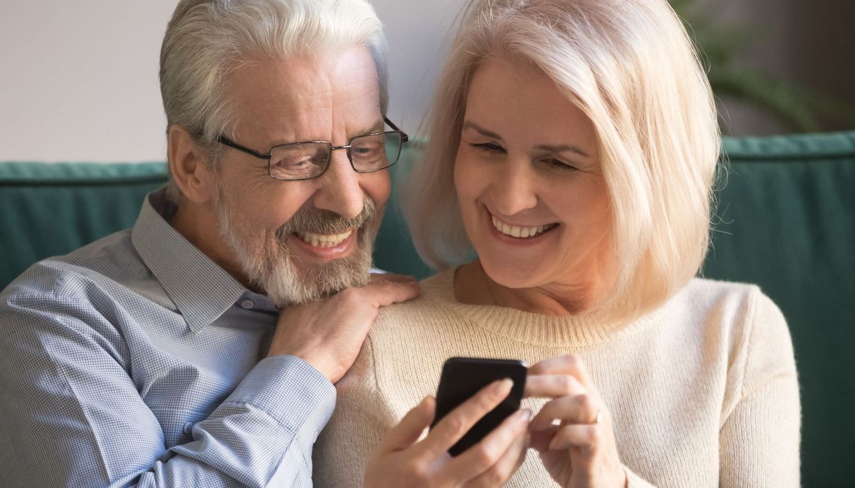 Älteres Paar schaut auf ein Smartphone.