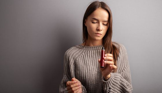 Junge Frau, hält eine E-Zigarette in der Hand und schaut diese fragend an.