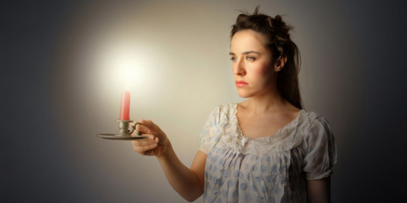 Junge Frau im Nachthemd trägt des Nachts eine Kerze vor sich her