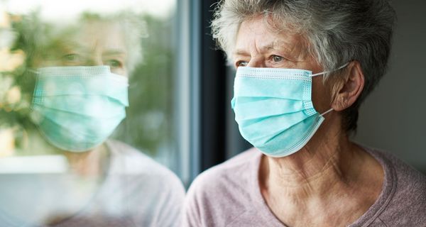 Seniorin mit Maske, schaut aus dem Fenster.