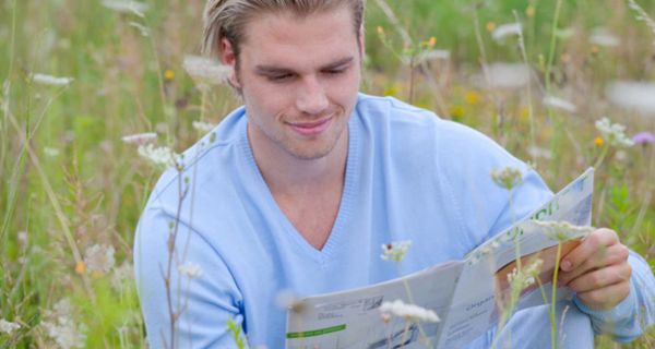 Mann sitzt auf einer Blumenwiese und liest