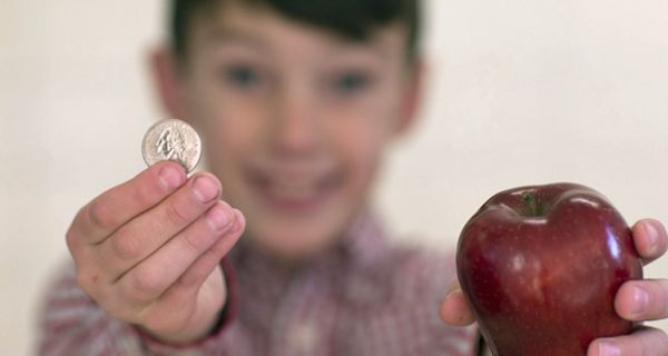 Junge hält eine Münze und einen Apfel ins Bild.