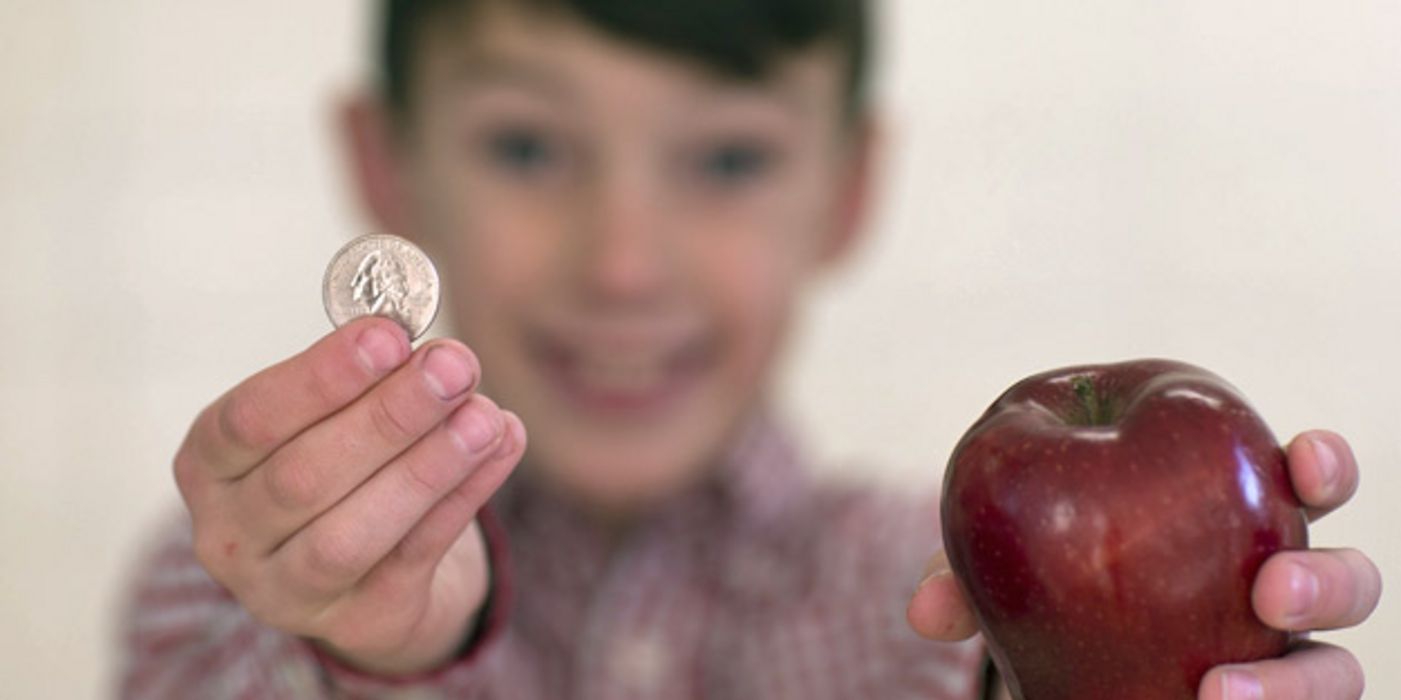 Junge hält eine Münze und einen Apfel ins Bild.