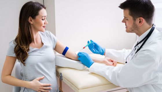 Ein Arzt nimmt einer schwangeren Frau Blut ab.