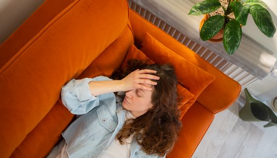 Erschöpfte Frau, liegt auf einer Couch.