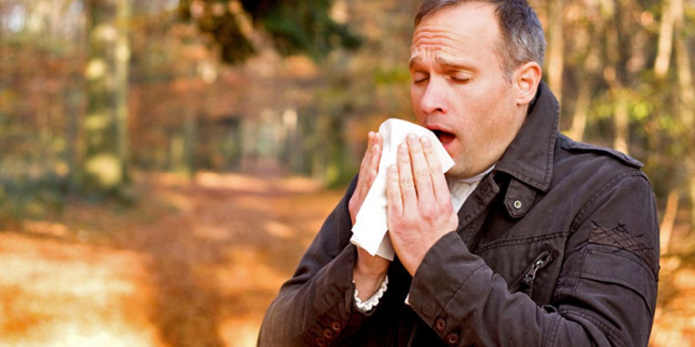 Mann im Mantel niest in ein Taschentuch.