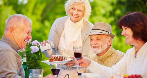 Sommer: Geburtstagsfeier draußen: 2 fröhliche Seniorenpaare feiern mit Geburtstagskuchen und Rotwein, stoßen gerade an mit Geburtstagskind