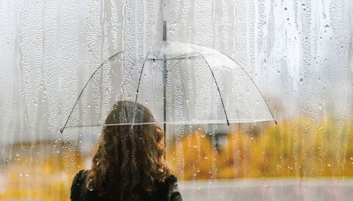 Frau von hinten mit Regenschirm, steht im Regen.