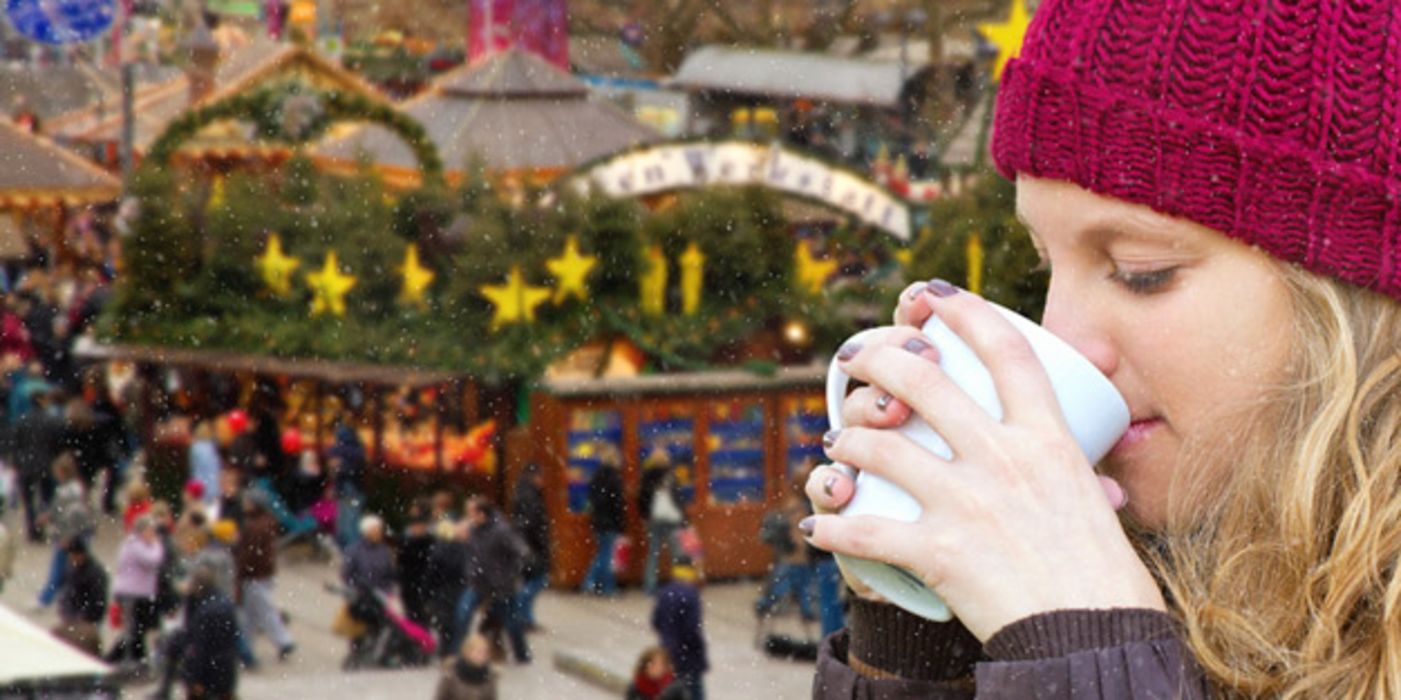 Junge Frau mit roter Mütze trinkt Glühwein.