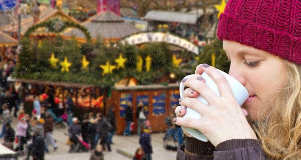 Junge Frau mit roter Mütze trinkt Glühwein.