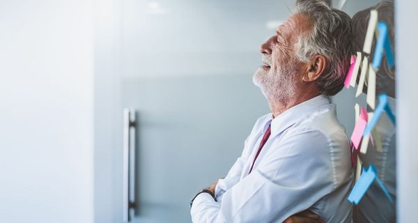 Senior, lehnt sich im Büro an die Wand und sieht erschöpft aus.