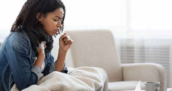 Junge Frau, sitzt auf der Couch und hustet.