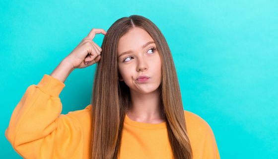 Mädchen mit langem Haar kratzt sich am Kopf.