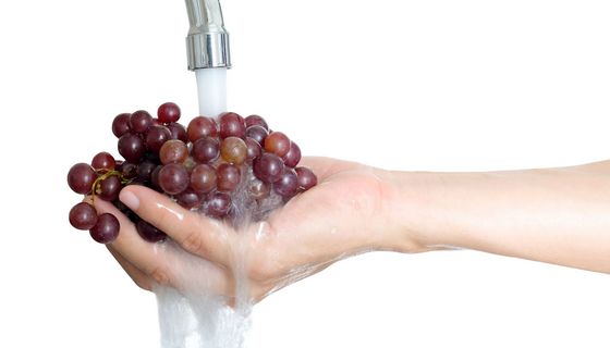 Hand mit Weintrauben unter Wasserhahn.