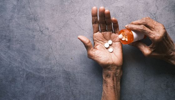Älterer Mann, schüttet sich aus einer Dose Tabletten in seine Hand.