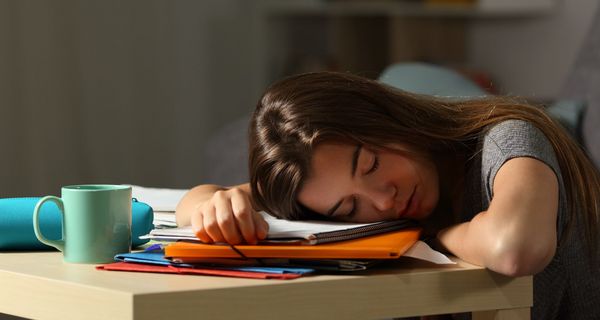 Junge Frau, legt ihren Kopf auf den Tisch und hat die Augen geschlossen.