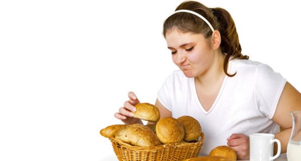 Leicht übergewichtige junge Frau greift zögerlich nach einem Brötchen aus einem Brotkorb