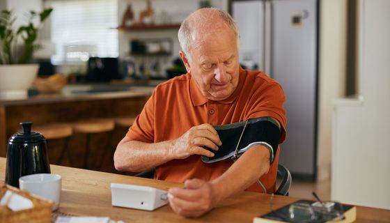 Älterer Herr zieht sich Blutdruckmanschette an, um sich den Blutdruck zu messen