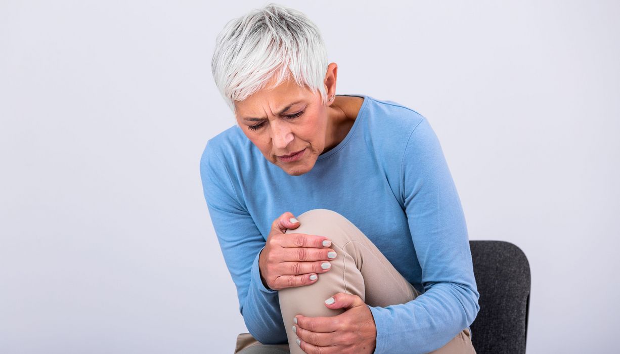 Ältere Frau, hält mit beiden Händen ihr Knie.
