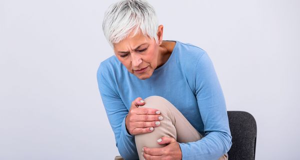 Ältere Frau, hält mit beiden Händen ihr Knie.