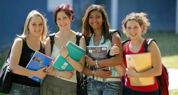 Vier jugendliche Mädchen stehen mit Schulsachen vor der Schule.