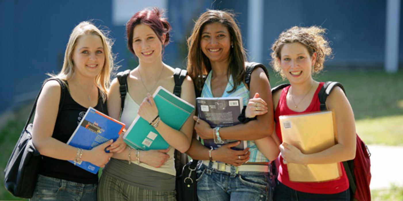 Vier jugendliche Mädchen stehen mit Schulsachen vor der Schule.