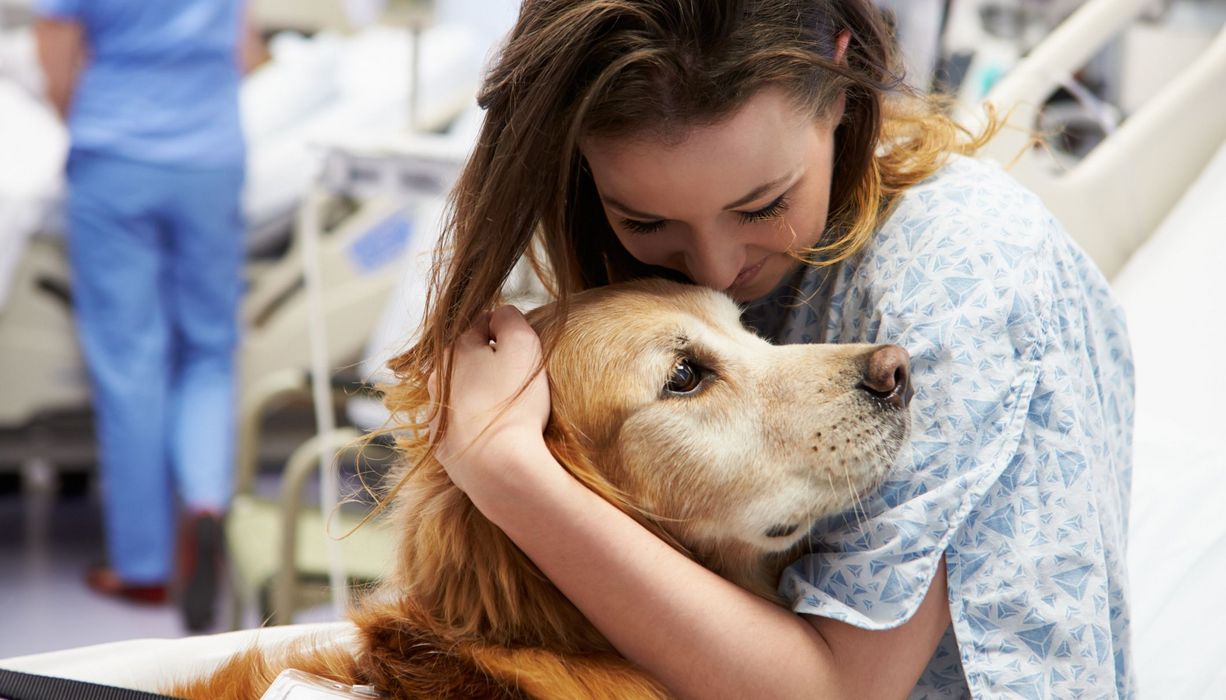 Junge Frau im Krankenhaus, umarmt einen Hund.